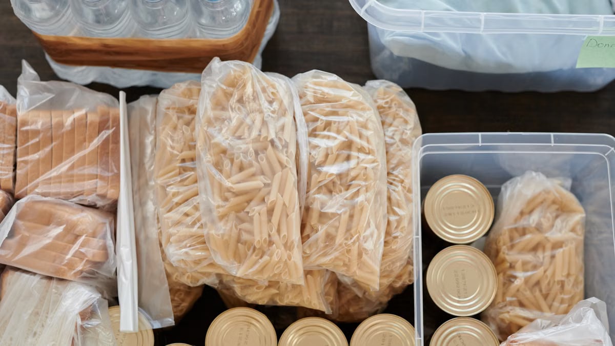 Aerial shot of pantry essentials including pasta, canned food, and bread packaged in plastic bags.